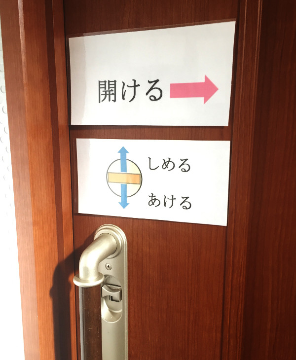 トイレの扉に貼られた、鍵の開閉方法を示した貼り紙と、扉を開ける方向を示した貼り紙。わかりにくい鍵のデザインを補っている。2016年に福島県相馬市で発見。